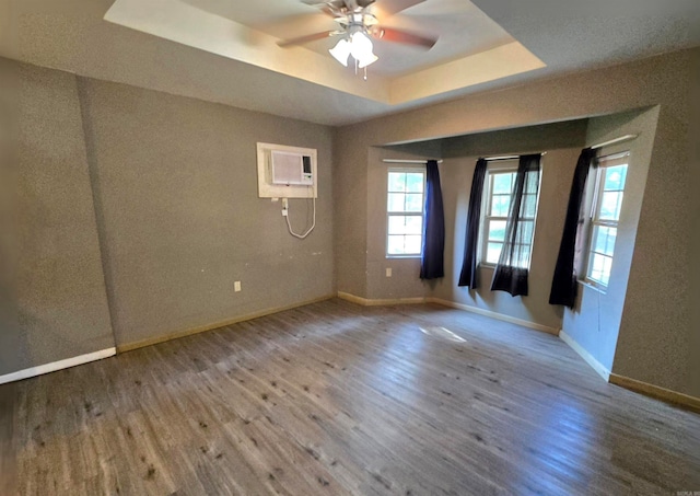 unfurnished room with a wall mounted AC, a tray ceiling, and hardwood / wood-style flooring