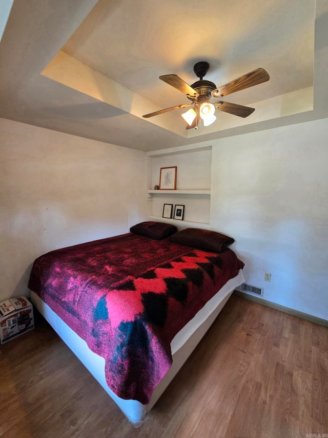 bedroom featuring ceiling fan, a raised ceiling, and wood-type flooring