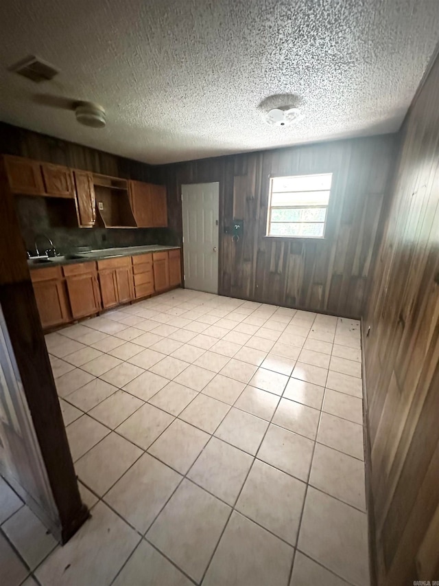 kitchen featuring wood walls, sink, light tile patterned floors, and a textured ceiling