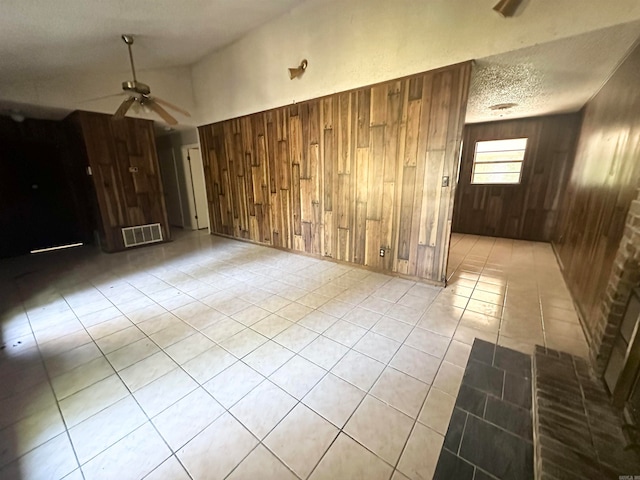 empty room with high vaulted ceiling, wooden walls, ceiling fan, light tile patterned floors, and a textured ceiling