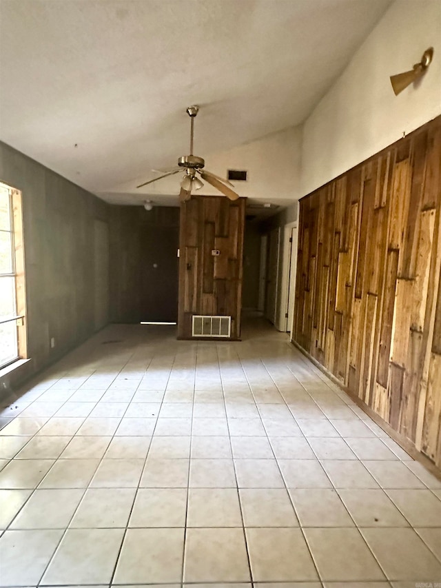 unfurnished living room featuring wood walls, lofted ceiling, light tile patterned floors, and ceiling fan