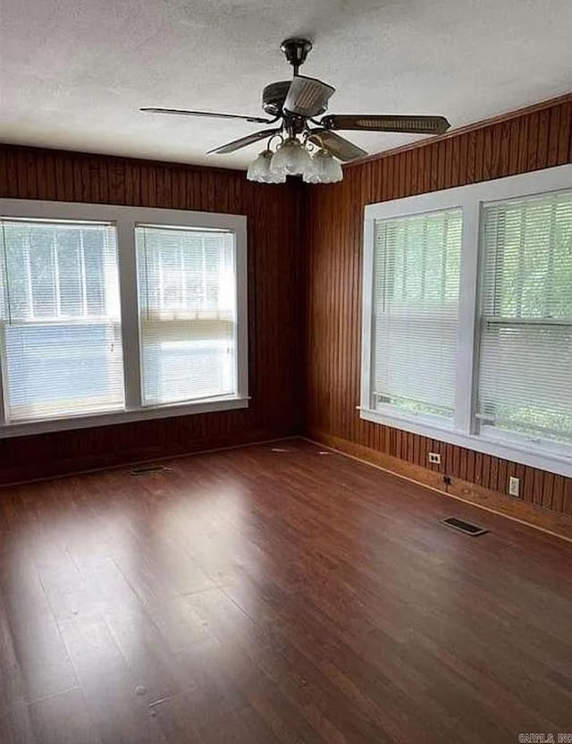 spare room featuring a textured ceiling, wooden walls, ceiling fan, and dark hardwood / wood-style flooring