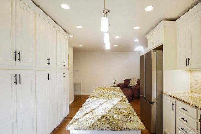 kitchen with stainless steel refrigerator, a kitchen island, decorative light fixtures, light stone countertops, and white cabinetry