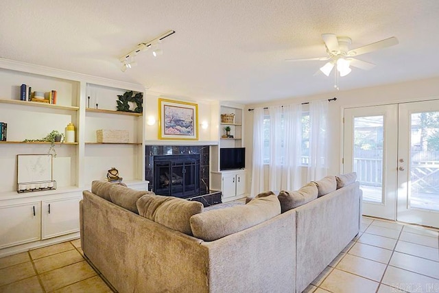 tiled living room featuring ceiling fan, built in features, french doors, a textured ceiling, and a premium fireplace