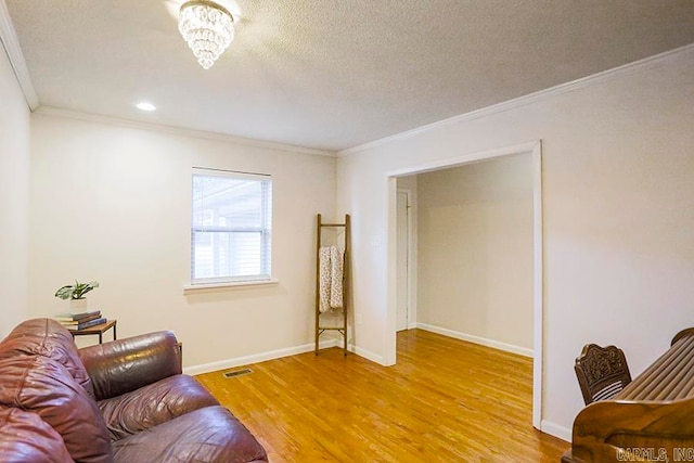 sitting room with crown molding, a chandelier, light wood-type flooring, and a textured ceiling