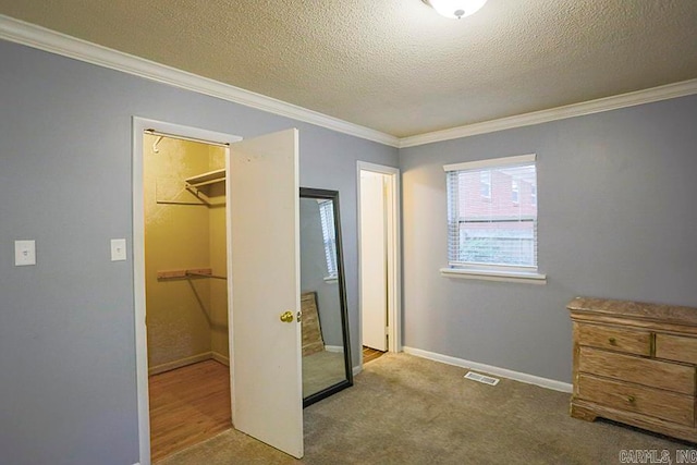 carpeted bedroom with a closet, crown molding, a walk in closet, and a textured ceiling