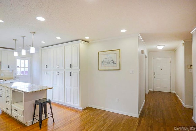 kitchen with light wood-type flooring, pendant lighting, light stone counters, white cabinets, and a center island