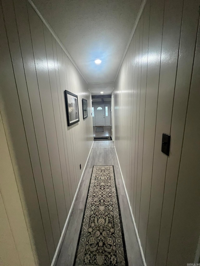 corridor with light hardwood / wood-style floors, crown molding, and wooden walls