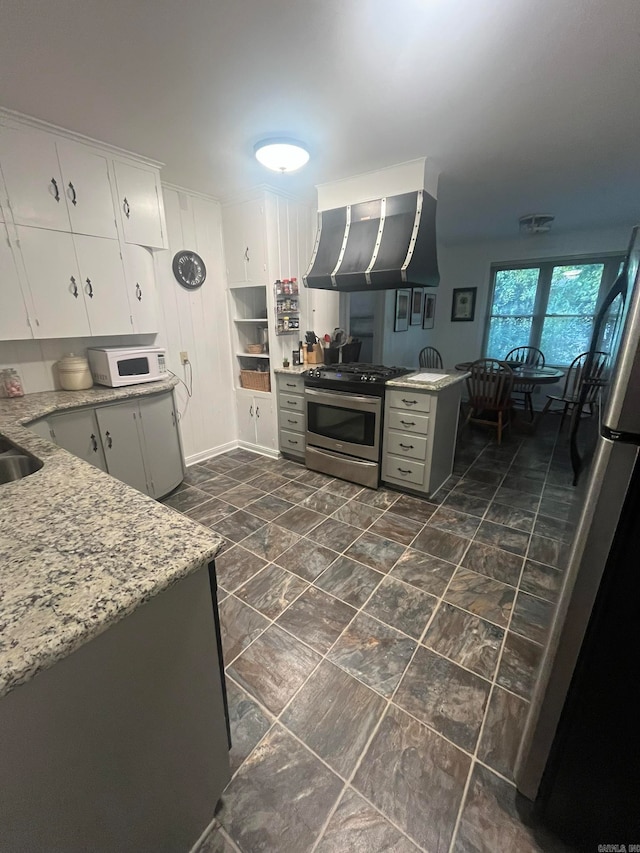 kitchen featuring light stone countertops, exhaust hood, white cabinets, fridge, and stainless steel gas range