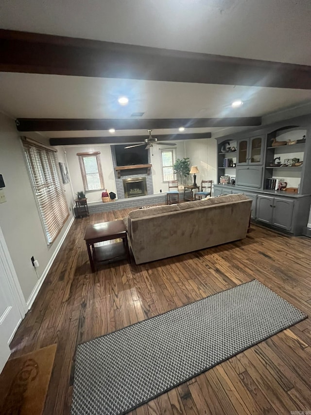 living room with a brick fireplace, beamed ceiling, dark hardwood / wood-style flooring, and ceiling fan