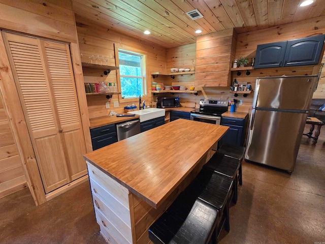 kitchen with blue cabinets, wooden counters, a kitchen island, wooden walls, and appliances with stainless steel finishes