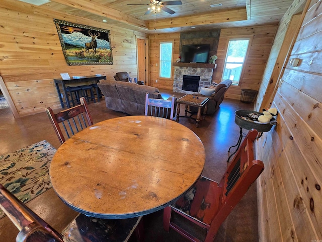 dining space with wooden walls, ceiling fan, a stone fireplace, and wooden ceiling