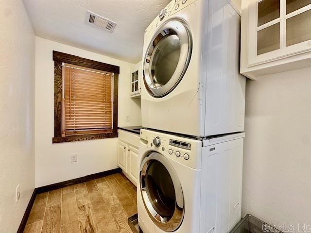 clothes washing area with cabinets and stacked washing maching and dryer