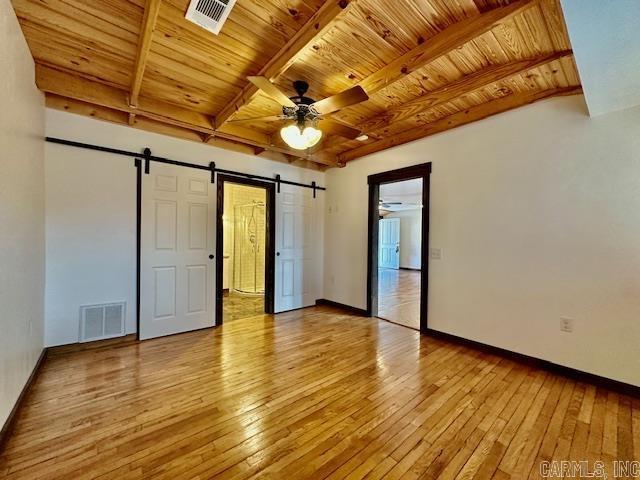 unfurnished bedroom featuring a barn door, beamed ceiling, wooden ceiling, and light wood-type flooring