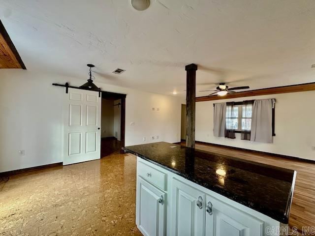 kitchen with a center island, white cabinets, ceiling fan, a barn door, and dark stone countertops