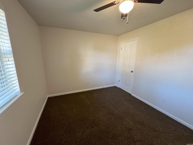 empty room featuring dark carpet, plenty of natural light, and ceiling fan