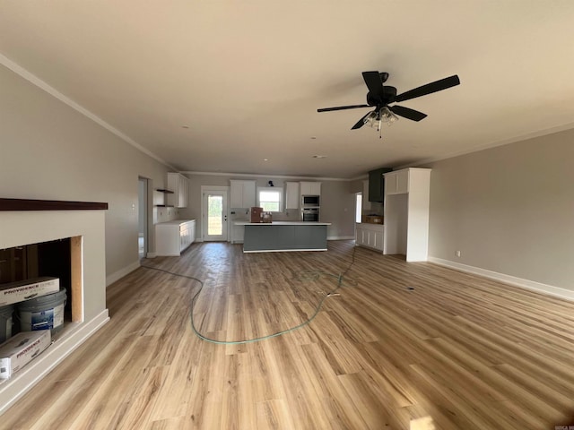 unfurnished living room featuring baseboards, ceiling fan, light wood-type flooring, and crown molding