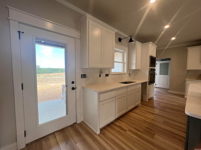 kitchen featuring built in microwave, light wood-type flooring, stainless steel oven, and white cabinetry