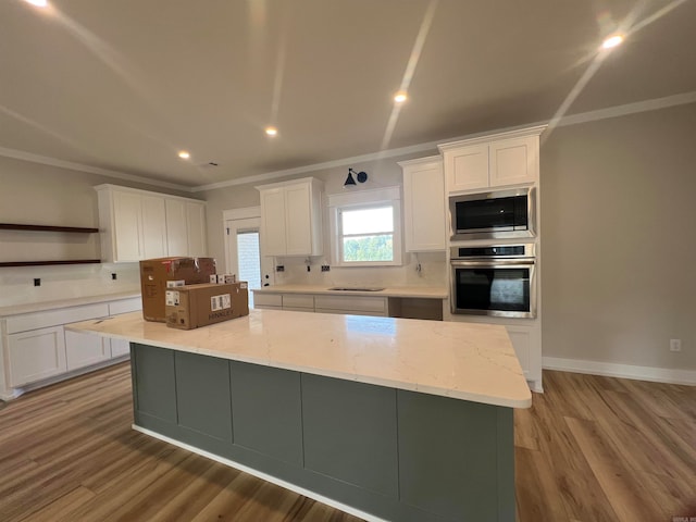 kitchen featuring a large island, stainless steel appliances, ornamental molding, white cabinets, and light stone countertops