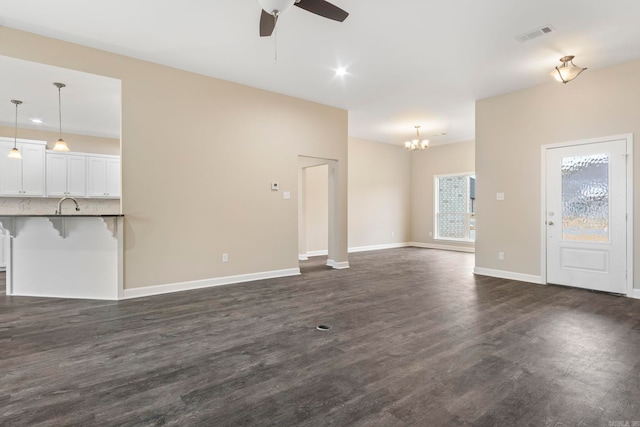 unfurnished living room with ceiling fan with notable chandelier, dark wood-type flooring, and sink