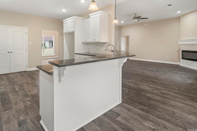 kitchen featuring a breakfast bar, a high end fireplace, white cabinets, hanging light fixtures, and dark hardwood / wood-style flooring