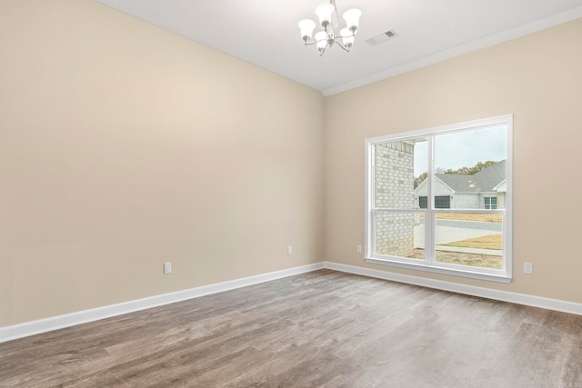 empty room featuring hardwood / wood-style flooring, an inviting chandelier, and crown molding