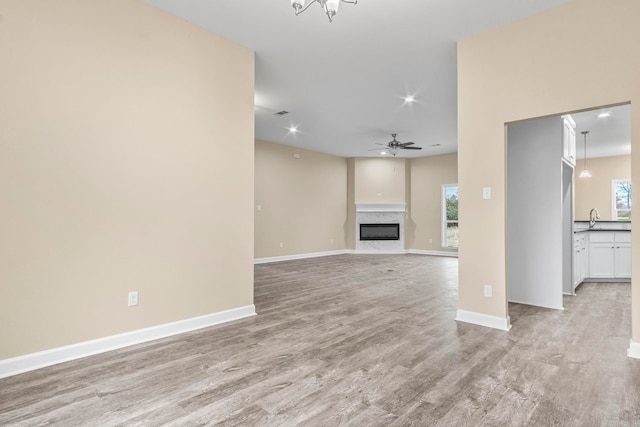 unfurnished living room featuring a wealth of natural light, light hardwood / wood-style flooring, a premium fireplace, and sink