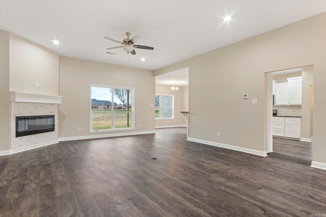 unfurnished living room with ceiling fan with notable chandelier, dark hardwood / wood-style flooring, and a fireplace