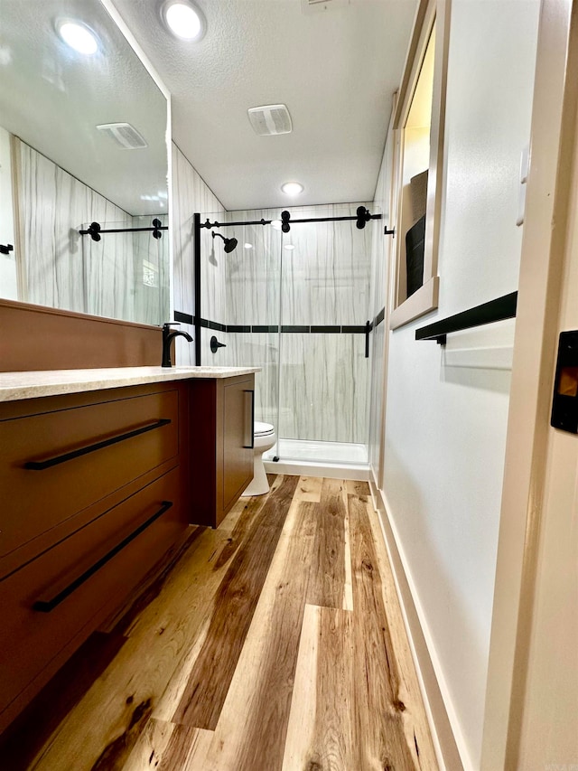 bathroom with vanity, wood-type flooring, tiled shower, toilet, and a textured ceiling