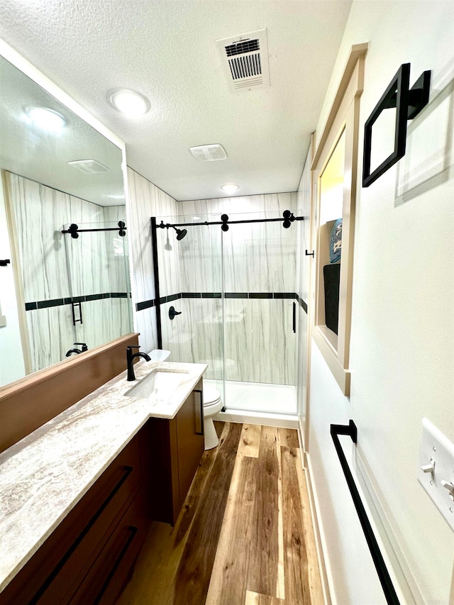 bathroom featuring vanity, walk in shower, hardwood / wood-style flooring, toilet, and a textured ceiling