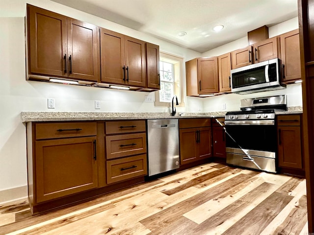 kitchen with light hardwood / wood-style floors, sink, stainless steel appliances, and light stone countertops