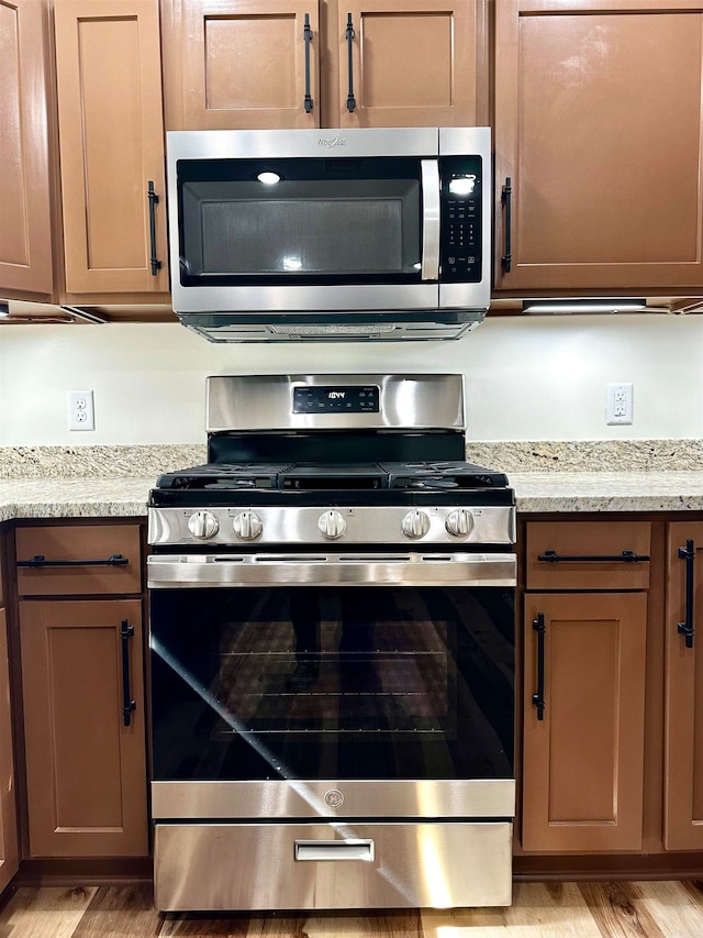 kitchen featuring light stone countertops, appliances with stainless steel finishes, and light wood-type flooring