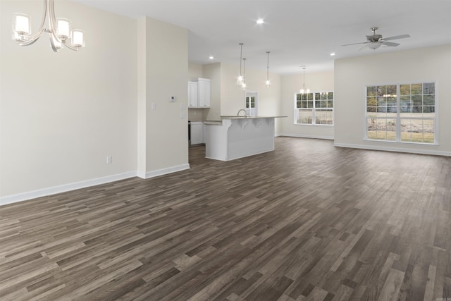 unfurnished living room featuring ceiling fan with notable chandelier and dark hardwood / wood-style floors