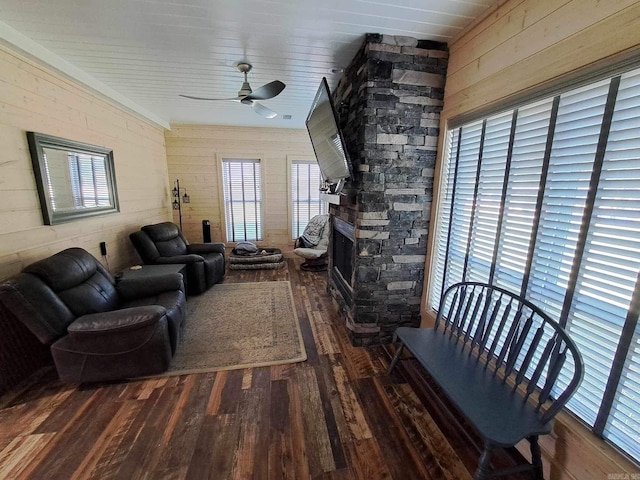 living room with ceiling fan, wooden ceiling, dark wood-type flooring, wooden walls, and a stone fireplace