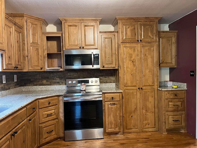 kitchen with light stone countertops, appliances with stainless steel finishes, wood-type flooring, and decorative backsplash