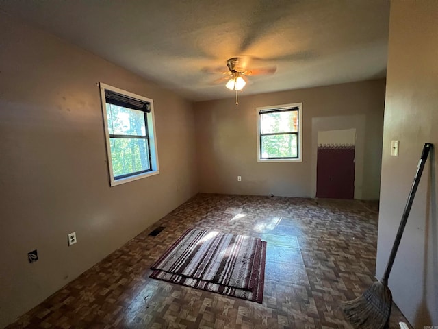 spare room featuring ceiling fan, a healthy amount of sunlight, and dark parquet flooring