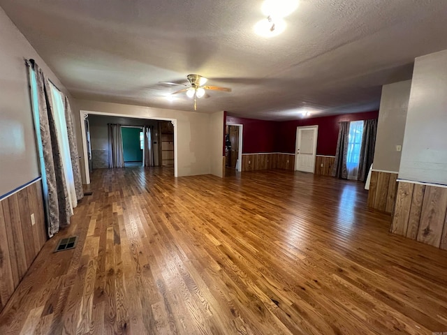 unfurnished room with wood walls, a textured ceiling, hardwood / wood-style flooring, and ceiling fan