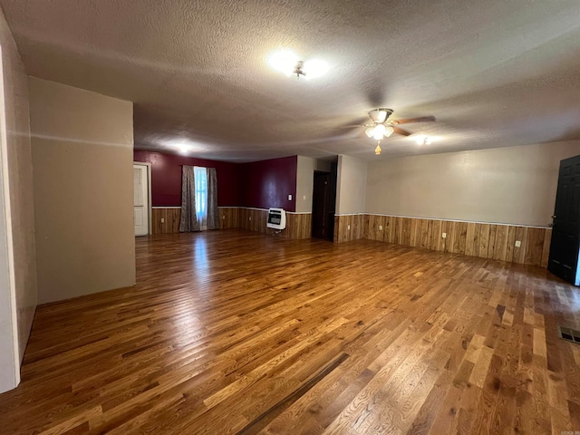 unfurnished living room with ceiling fan, wood walls, a textured ceiling, and hardwood / wood-style floors