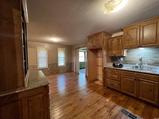 kitchen featuring tasteful backsplash, light stone counters, a textured ceiling, wood-type flooring, and sink