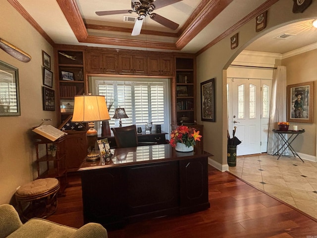 office space featuring built in shelves, ceiling fan, crown molding, hardwood / wood-style floors, and a raised ceiling