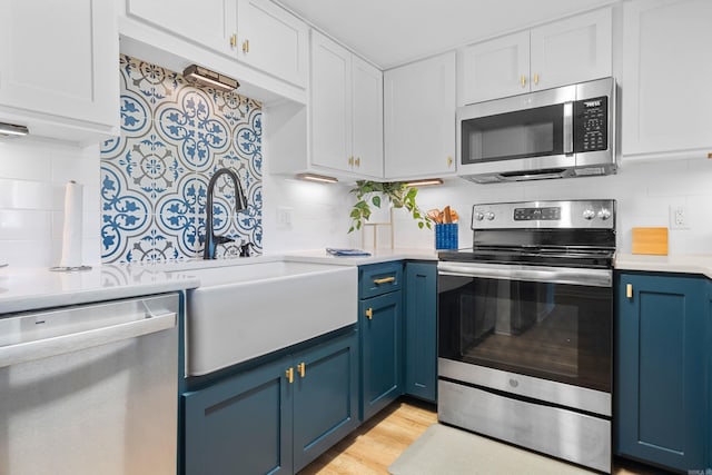 kitchen with appliances with stainless steel finishes, blue cabinets, backsplash, and white cabinets