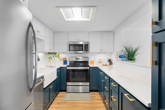 kitchen with blue cabinetry, white cabinets, appliances with stainless steel finishes, and light hardwood / wood-style flooring