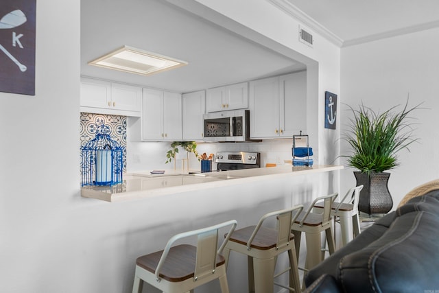 kitchen with crown molding, a breakfast bar, kitchen peninsula, appliances with stainless steel finishes, and white cabinetry