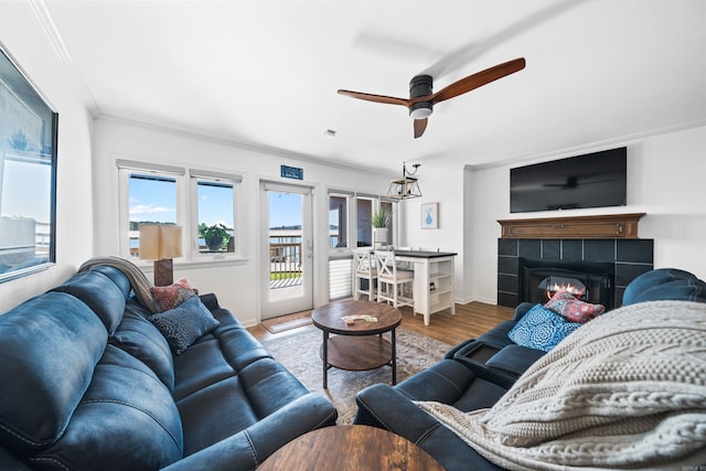 living room with ceiling fan, crown molding, a tiled fireplace, and hardwood / wood-style floors