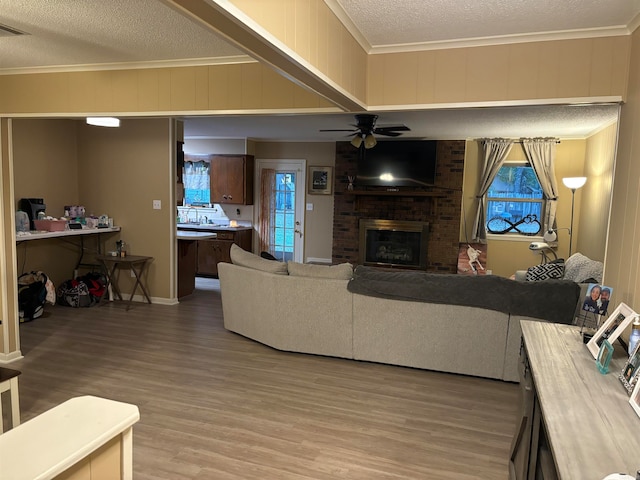 living room featuring hardwood / wood-style floors, ceiling fan, ornamental molding, a fireplace, and a textured ceiling