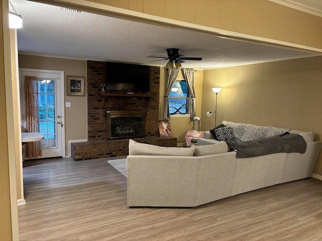 living room featuring a brick fireplace, ceiling fan, a textured ceiling, and light wood-type flooring