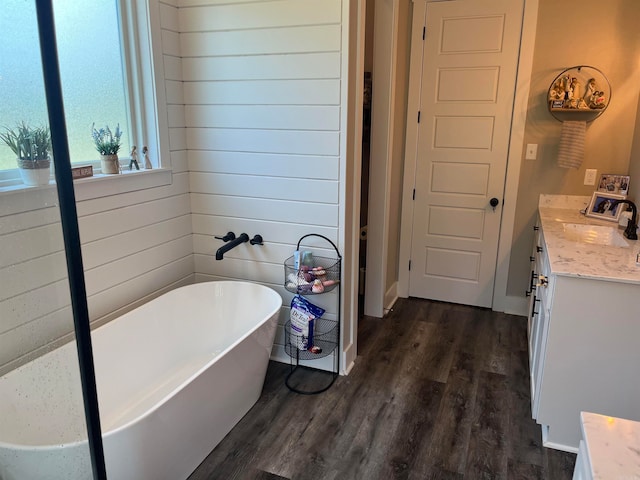 bathroom with wood walls, wood-type flooring, a bathtub, and vanity