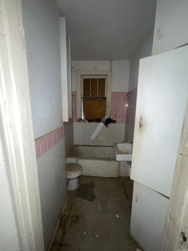 bathroom featuring a tub, tile walls, sink, and toilet