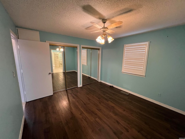 unfurnished bedroom featuring a textured ceiling, ceiling fan, multiple closets, and dark hardwood / wood-style flooring