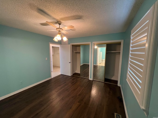 unfurnished bedroom with ceiling fan, multiple closets, a textured ceiling, and dark hardwood / wood-style floors